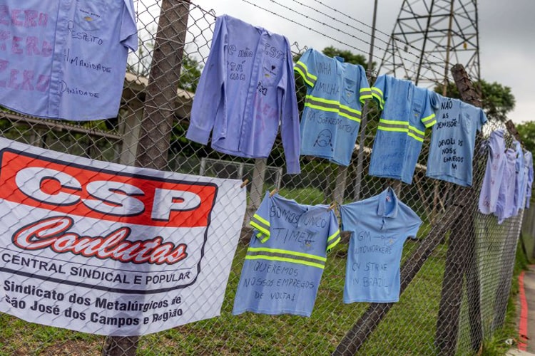 Em protesto contra demissões, trabalhadores da GM penduram uniformes em frente à fábrica